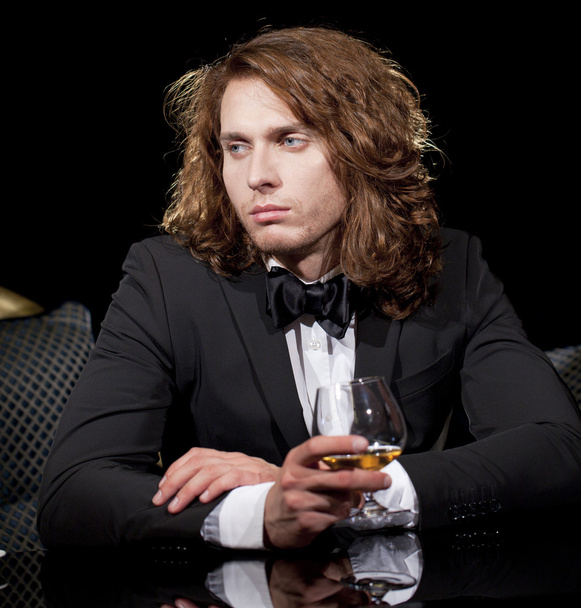 Elegant young man holding a glass of brandy looking away - Photo, image
