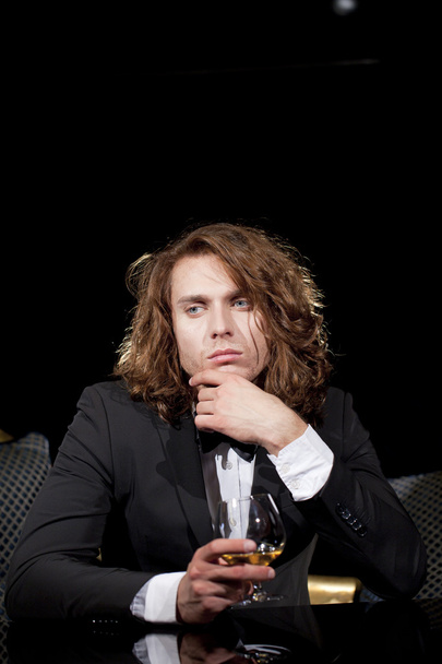 Elegant young man holding a glass of brandy looking away - Zdjęcie, obraz