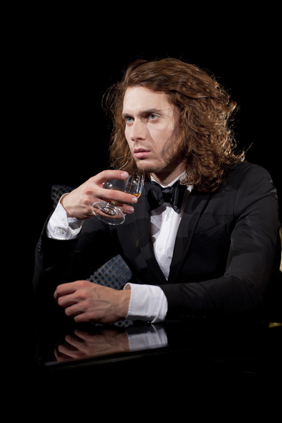Elegant young man holding a glass of brandy looking away - Фото, зображення