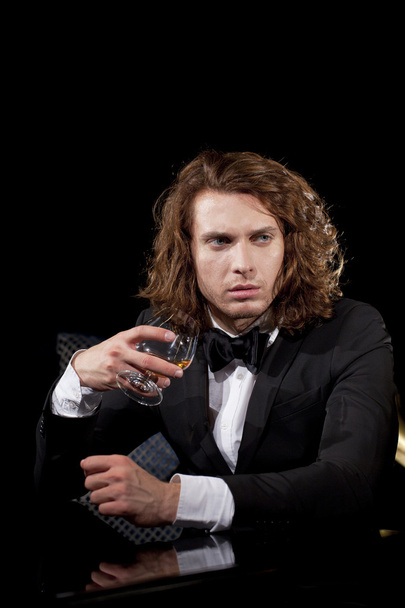 Elegant young man holding a glass of brandy looking away - Фото, зображення