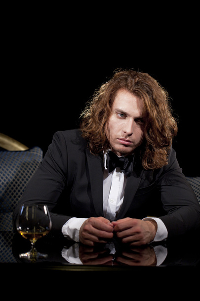 Elegant young man holding a glass of brandy looking away - Fotoğraf, Görsel