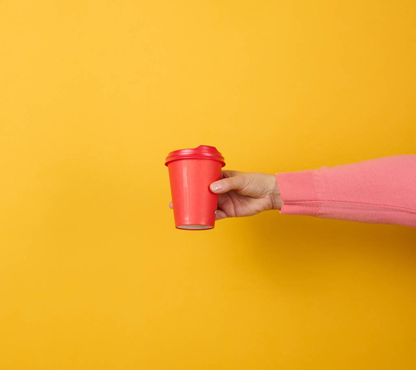 hand holds paper cardboard red cup for coffee, yellow background. Eco-friendly tableware - 写真・画像