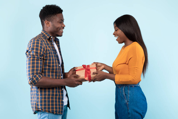 Happy black couple holding giving gift box at blue studio - Valokuva, kuva