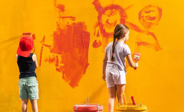 Kaksi lasta pitelemässä siveltimiä käsissään ja maalaamassa seinää huoneessa. - Valokuva, kuva