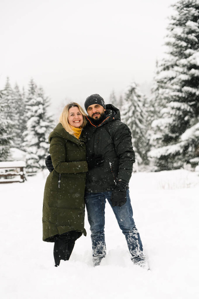 Attractive man and woman cuddling in the frosty forest. Adult couple in puffer jacket have fun on walk. Romantic date in winter time.Winter lovestory - Foto, Bild