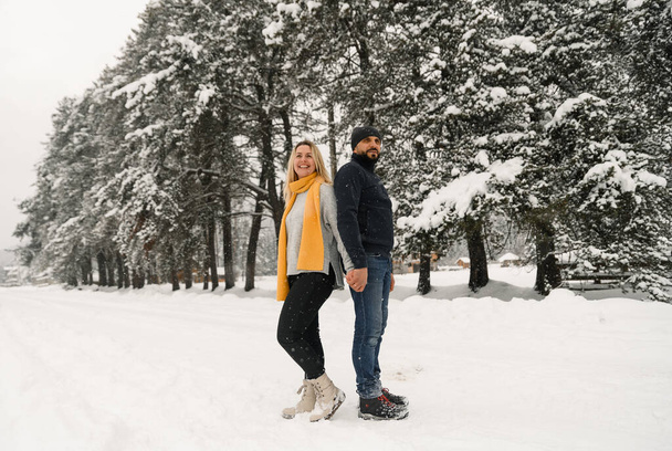 Attractive man and woman cuddling in the frosty forest. Adult couple in sweaters have fun on walk. Romantic date in winter time.Winter lovestory - Φωτογραφία, εικόνα