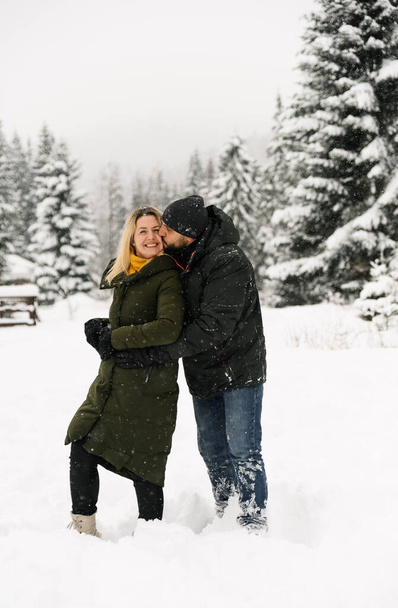 Attractive man and woman cuddling in the frosty forest. Adult couple in puffer jacket have fun on walk. Romantic date in winter time.Winter lovestory - Fotoğraf, Görsel