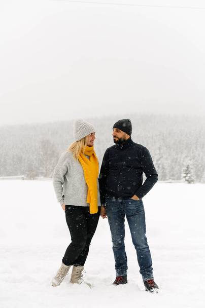 Attractive man and woman cuddling in the frosty forest. Adult couple in sweaters have fun on walk. Romantic date in winter time.Winter lovestory - Foto, afbeelding