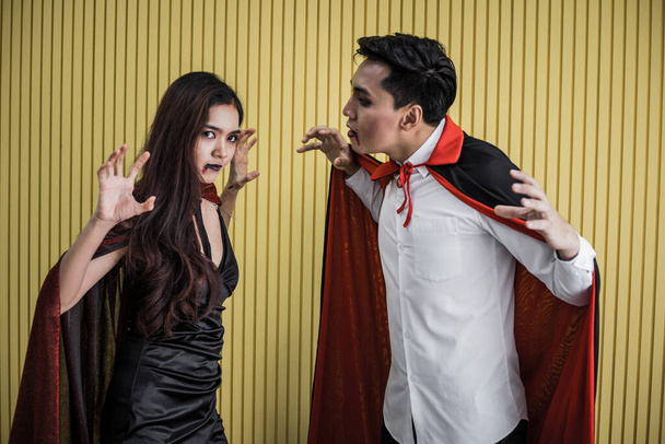 Halloween concept of young Asian woman in costume witch and Asian man in costume dracula on yellow background. Portrait teen couple dressed up as witches and dracula for celebrate  Halloween festival. - Foto, Bild