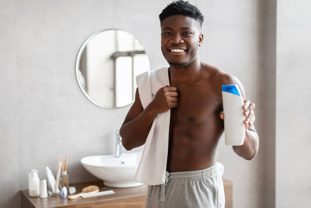 Black Guy Holding Shampoo Bottle Advertising Male Product In Bathroom - Foto, afbeelding
