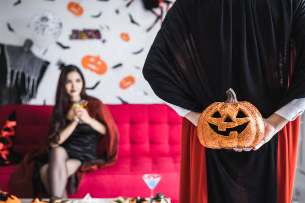 Boyfriend in the Dracula costume surprised his girlfriend by holding an orange Halloween pumpkin behind, with a girlfriend background that was anticipating the gift he received from her boyfriend. - Photo, Image