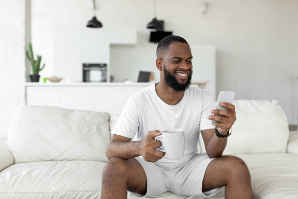 Black man using his smartphone drinking coffee - Valokuva, kuva