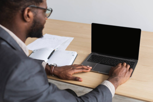 Millennial empresario negro que trabaja en PC portátil con pantalla en blanco en la oficina, maqueta para el sitio web - Foto, imagen