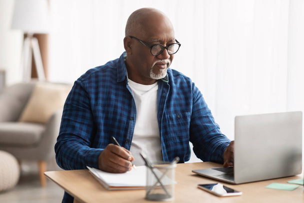 Black Man Using Laptop Taking Notes In Office, Wearing Eyeglasses - Zdjęcie, obraz