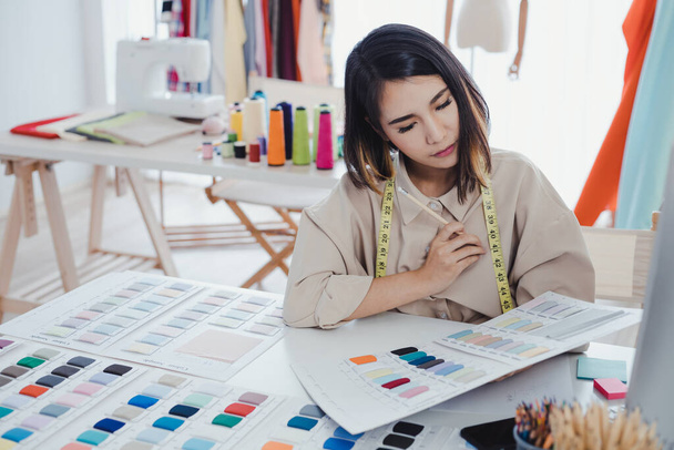 Femme designer asiatique réfléchissent et conçoivent des vêtements pour les clients commander des articles au bureau du concepteur dans le studio. Les créateurs de vêtements travaillent dans le bureau. Concept de créateur de start-up. - Photo, image