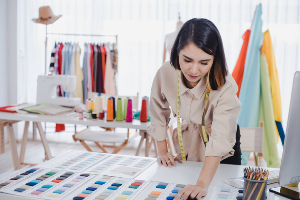 Asian woman designer are thinking and designing clothes for customers order items at the designer desk in the studio. Clothes designers are working in the office. Startup designer concept. - Фото, зображення