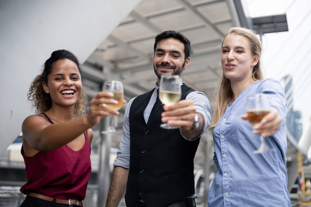 Οι επιχειρηματίες τσούζουν ποτήρια και πίνουν κρασί για να γιορτάσουν την επιτυχημένη δουλειά. Ομάδα επιχειρηματιών γιορτάζουν πίνοντας κρασί με χαμόγελο. - Φωτογραφία, εικόνα