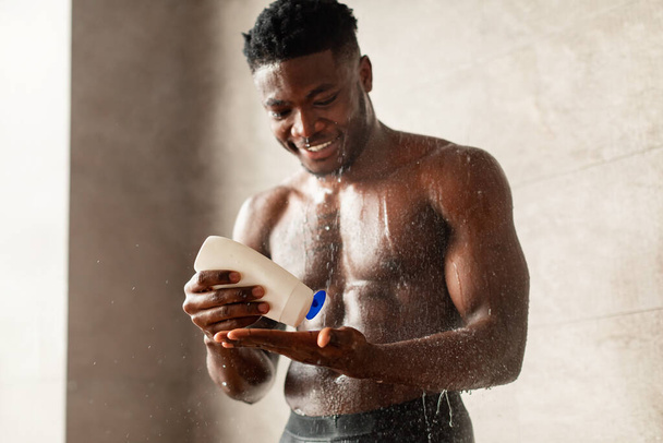 アフリカ系アメリカ人男性手にシャンプーをかけるシャワー室内 - 写真・画像