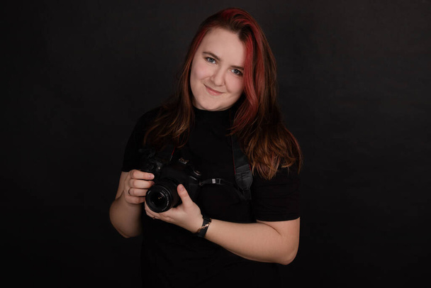redhead girl with a professional camera posing on black background. woman female photographer.  - Valokuva, kuva