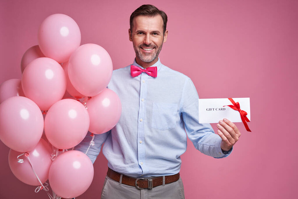 Caucasian mature man holding pink balloons and a gift card - Фото, изображение