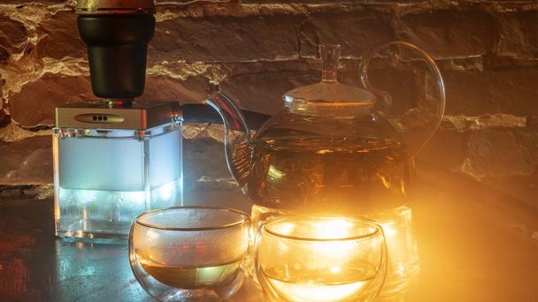 A pot of tea with herbs and smoking hookah on a dark red brick wall background. - Valokuva, kuva