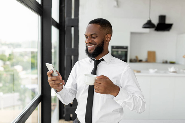 Black guy texting on his smartphone drinking coffee - Fotografie, Obrázek
