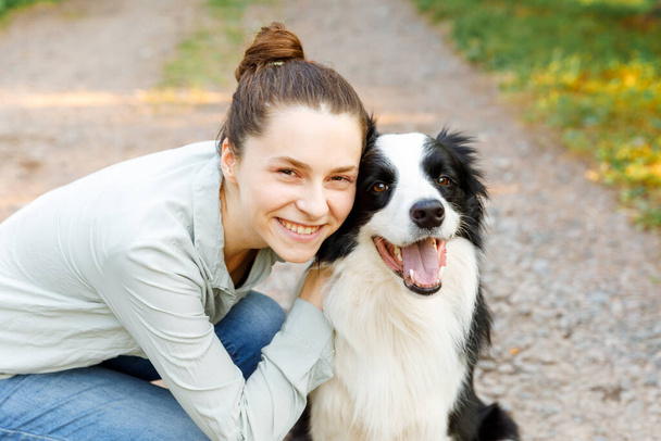 Smiling young attractive woman playing with cute puppy dog border collie on summer outdoor background. Girl holding embracing hugging dog friend. Pet care and animals concept. - Photo, Image