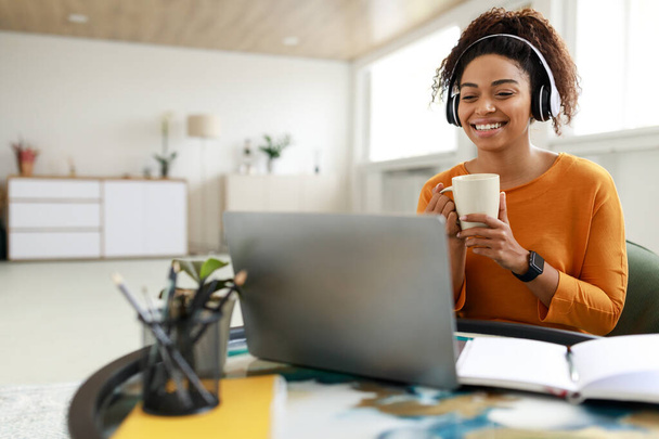 Χαμογελώντας μαύρη κυρία βλέποντας βίντεο στον υπολογιστή, πίνοντας καφέ - Φωτογραφία, εικόνα