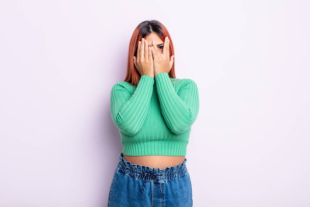 young hispanic woman covering face with hands, peeking between fingers with surprised expression and looking to the side - Фото, изображение