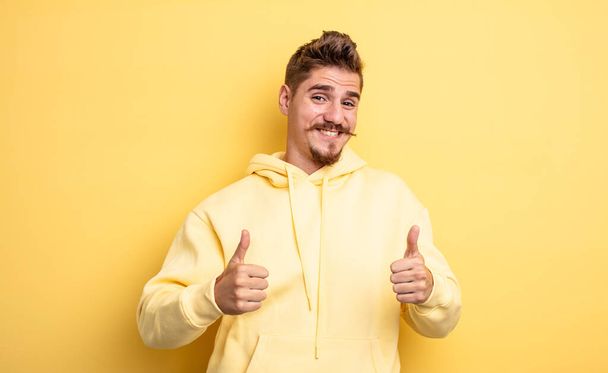 young handsome man smiling broadly looking happy, positive, confident and successful, with both thumbs up. strange moustache concept - Foto, immagini
