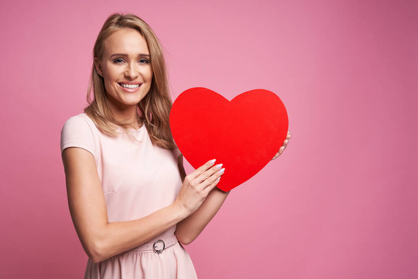 Caucasian ethnicity woman on pink background holding wooden heart - Foto, afbeelding