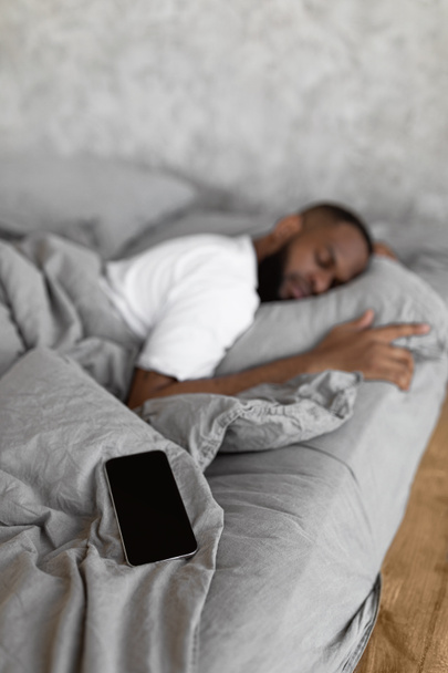 Jeune homme afro-américain dormant au lit avec téléphone portable - Photo, image