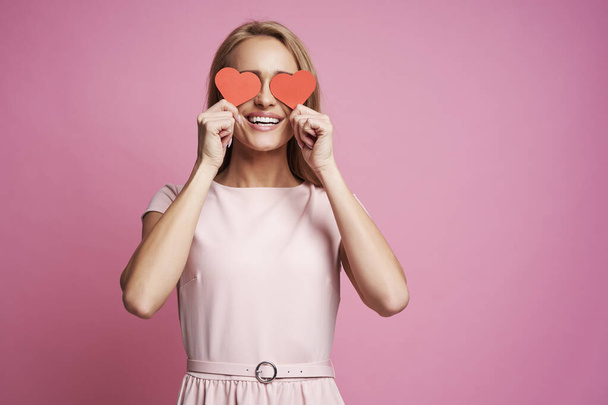 Attractive caucasian woman covering eyes with small red hearts  - Photo, Image
