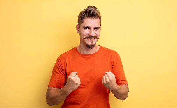 young handsome man shouting triumphantly, laughing and feeling happy and excited while celebrating success. strange moustache concept - Foto, Imagem