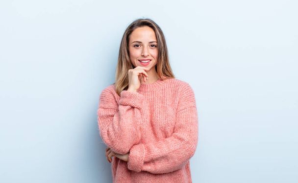 pretty caucasian woman looking happy and smiling with hand on chin, wondering or asking a question, comparing options - 写真・画像