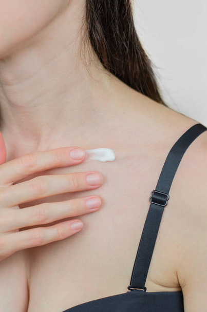 Una mujer se aplica crema hidratante en la clavícula. Cuidado de la piel. Hidratar la piel en invierno - Foto, imagen