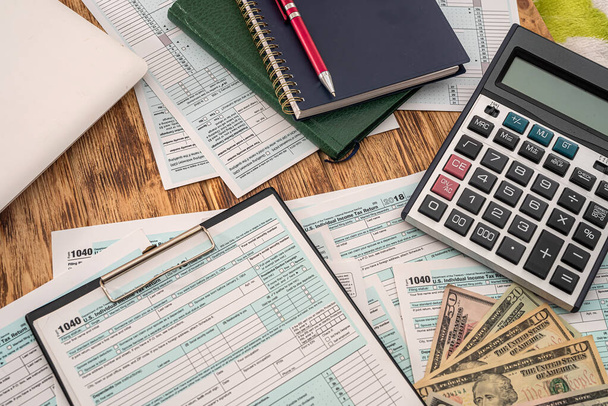 on the table are tax forms 1040 with dollars, coins, calculator, notebook and pen. Business concept - 写真・画像