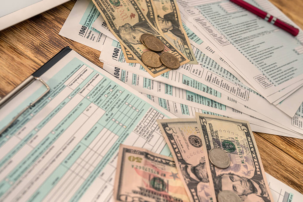 σε ένα ξύλινο τραπέζι βρίσκονται αμερικανικές φορολογικές δηλώσεις, χαρτονομίσματα αμερικανικών δολαρίων και ένα στυλό. Επιχειρηματική έννοια - Φωτογραφία, εικόνα