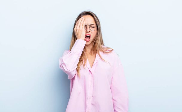 pretty caucasian woman looking sleepy, bored and yawning, with a headache and one hand covering half the face - Foto, Imagen