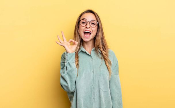 pretty caucasian woman feeling successful and satisfied, smiling with mouth wide open, making okay sign with hand - 写真・画像