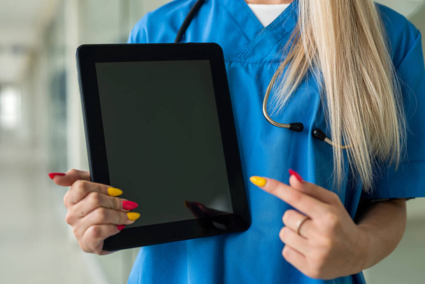 young beautiful nurse stands in uniform in the hallway and reads a tablet. Medicine concept - Foto, Imagen