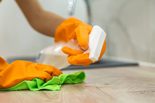 Mujer con guantes amarillos limpia la superficie de pie en la cocina. Servicios de limpieza concepto de desinfección - Foto, Imagen