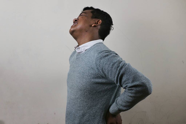 an asian man is holding his waist in pain and his face shows that he is enduring the pain - Photo, Image