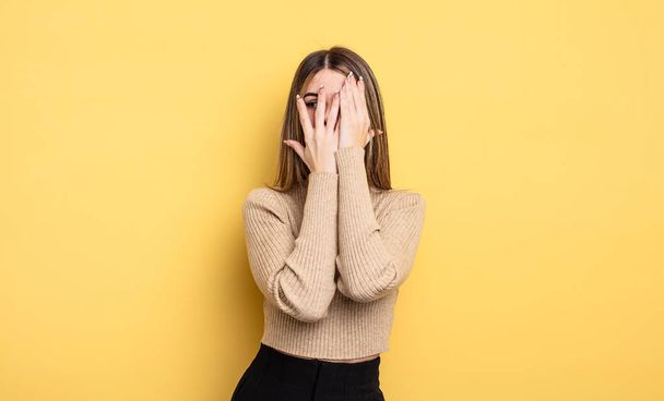 pretty caucasian woman covering face with hands, peeking between fingers with surprised expression and looking to the side - Photo, image