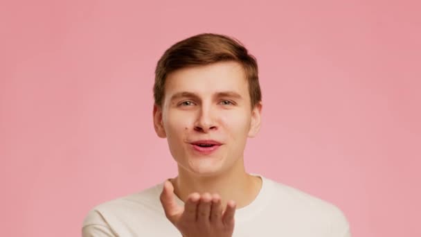 Παιχνιδιάρης τύπος φυσάει ένα φιλί χαμογελώντας ποζάροντας πάνω από ροζ φόντο - Πλάνα, βίντεο