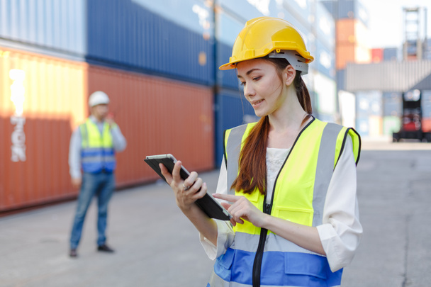 Women worker use tablet in uniform wearing safety helmet using laptop checking containers loading. Area logistics import export and shipping. - Фото, зображення