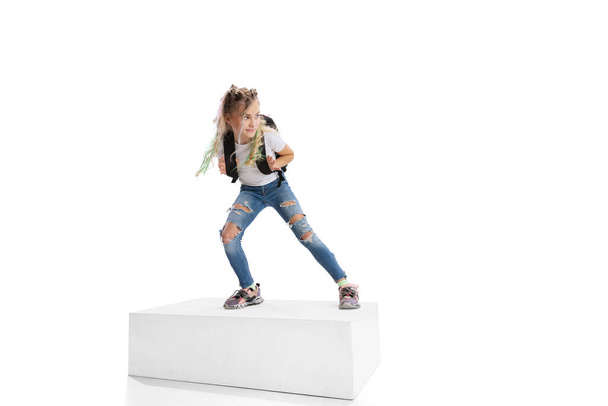Full-length portrait of smiling girl in casual clothes standing on big box isolated on white studio background. Happy childhood concept. - Foto, Imagem