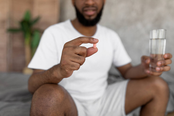 Black man taking pills holding glass of water - Фото, изображение