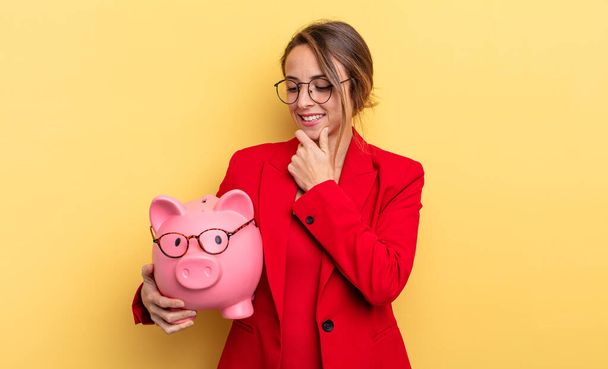 businesswoman smiling with a happy, confident expression with hand on chin. piggy bank concept - Foto, Imagem