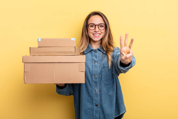 pretty woman smiling and looking friendly, showing number three. package boxes concept - Fotoğraf, Görsel